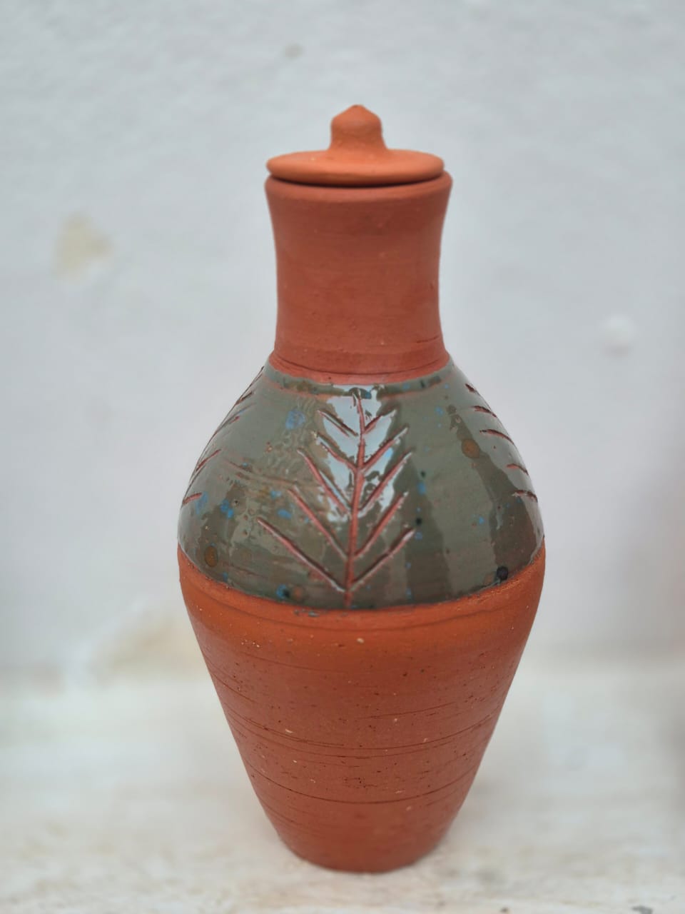 جره بطلاء زجاجي اخضر مع غطاء و مزخرفة بحفر غائر بتصميم سعف النخيل